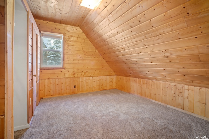 Bonus room featuring light carpet, lofted ceiling, wood walls, and wooden ceiling