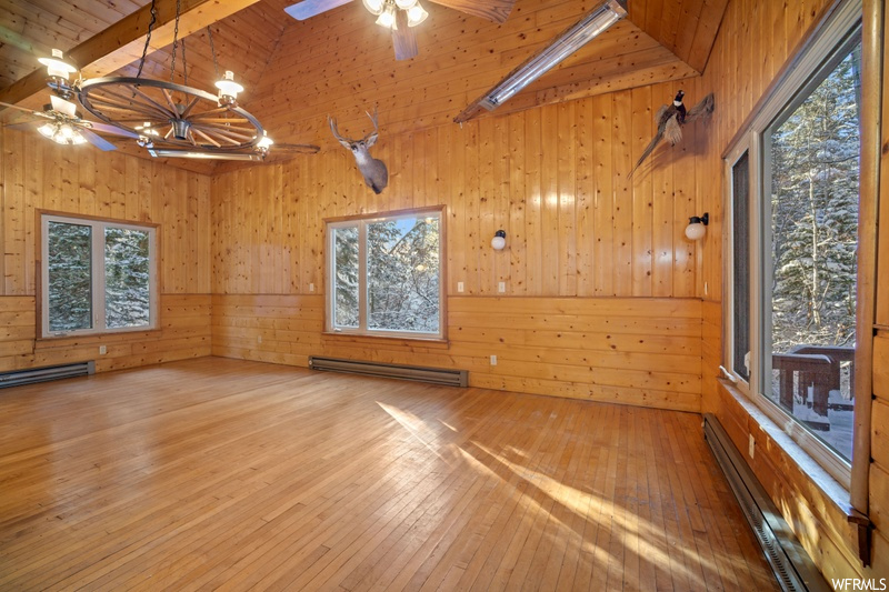 Spare room featuring beamed ceiling, wooden walls, wood ceiling, wood-type flooring, and a baseboard heating unit