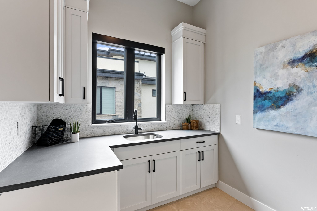 Kitchen with light tile flooring, white cabinets, tasteful backsplash, and sink
