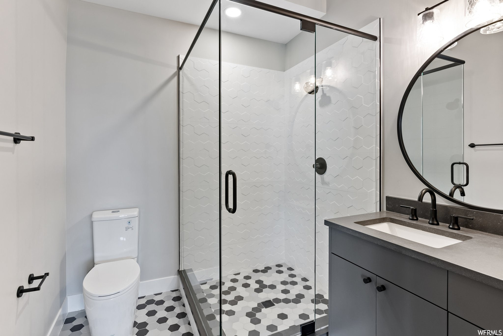 Bathroom featuring tile flooring, a shower with shower door, toilet, and oversized vanity