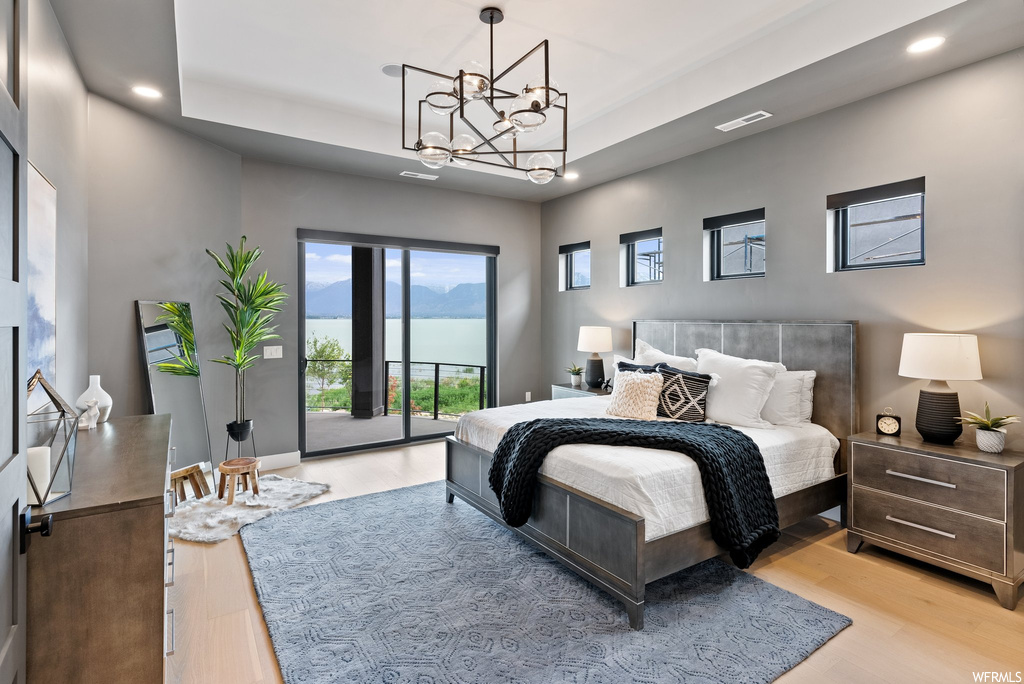 Bedroom featuring light hardwood / wood-style floors, access to outside, a raised ceiling, and a notable chandelier