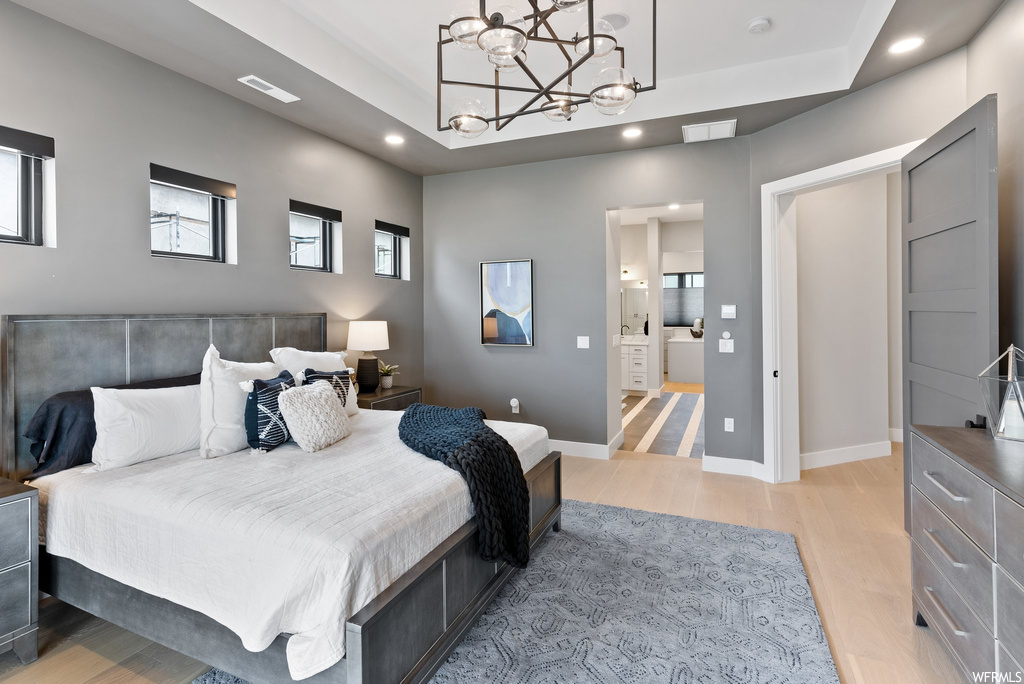 Bedroom featuring a tray ceiling, ensuite bath, light wood-type flooring, and an inviting chandelier