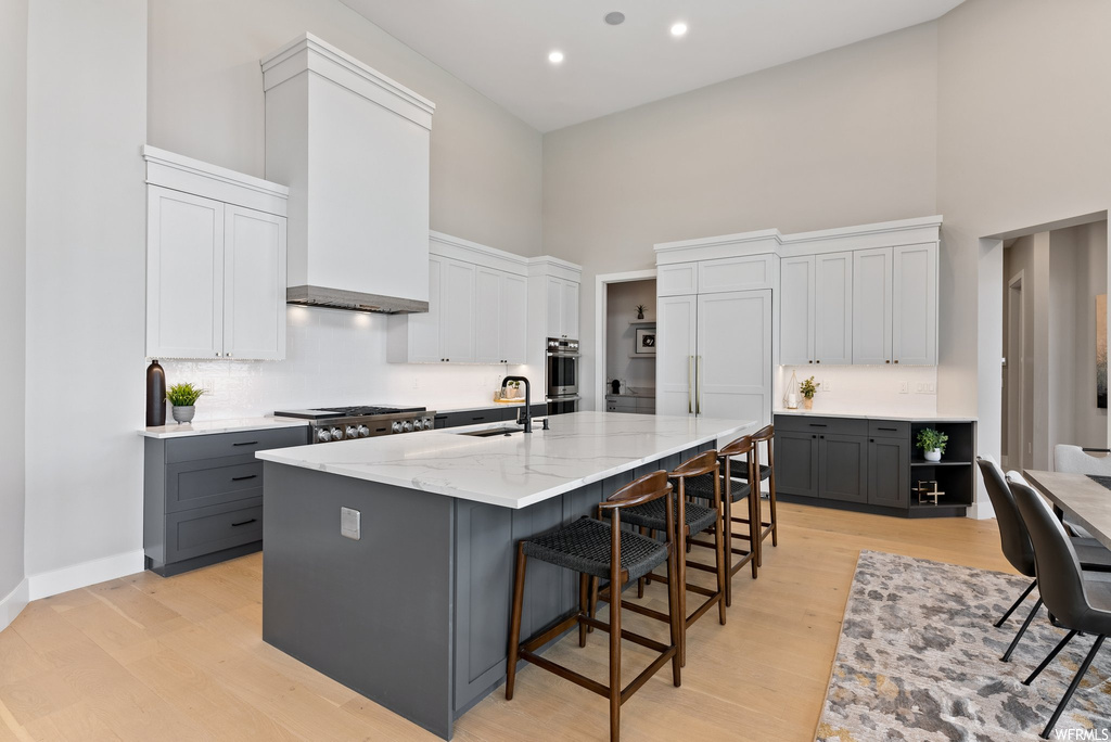Kitchen featuring a kitchen island with sink, a towering ceiling, gray cabinetry, and a breakfast bar