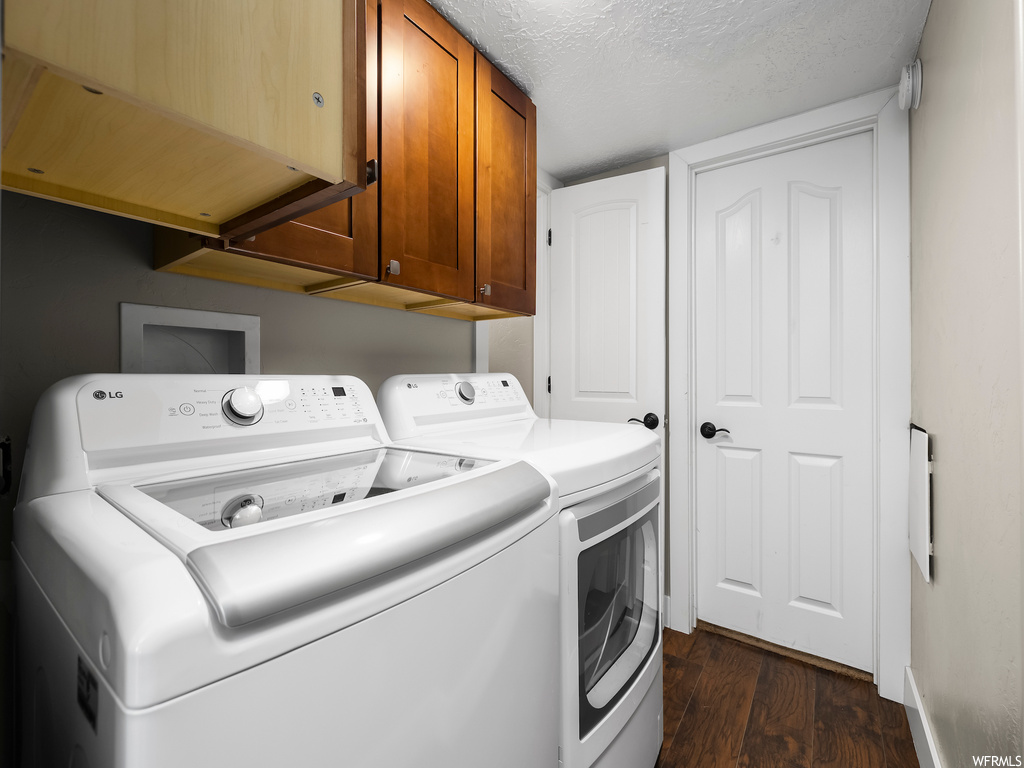 Laundry room with washer and dryer, a textured ceiling, hookup for a washing machine, dark hardwood / wood-style flooring, and cabinets