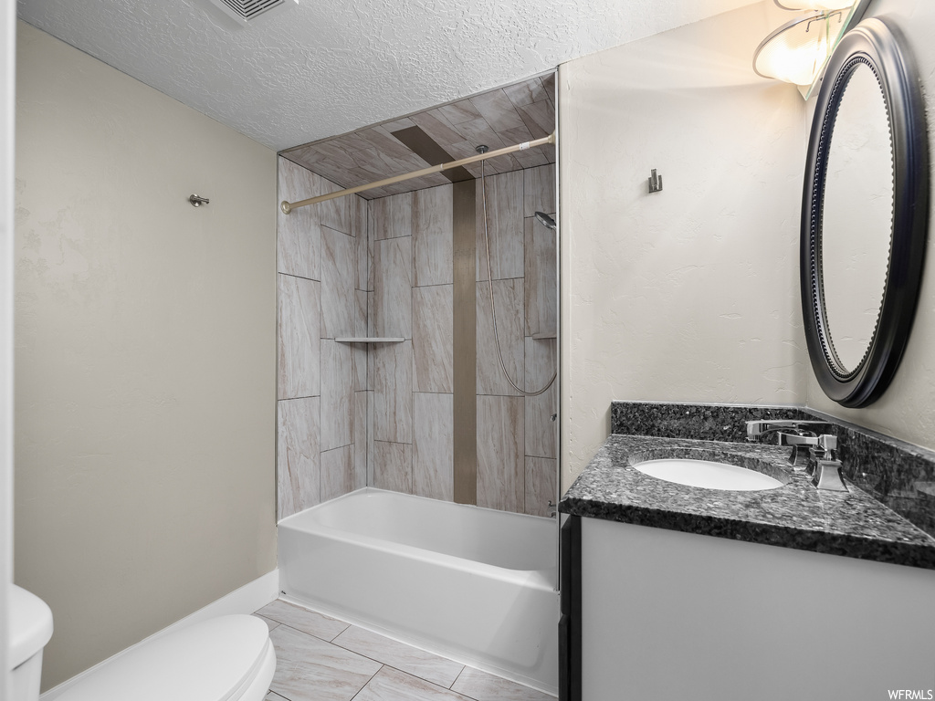 Full bathroom featuring a textured ceiling, toilet, vanity with extensive cabinet space, bathtub / shower combination, and tile floors