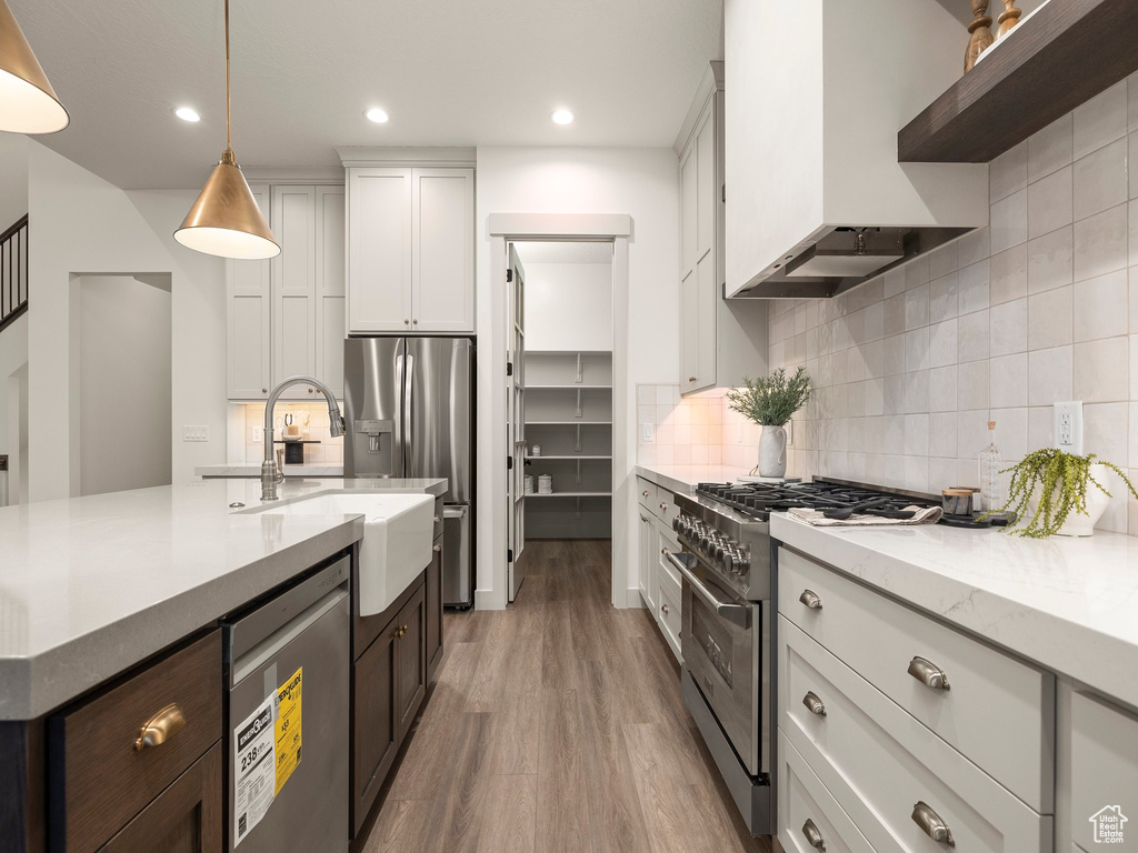 Kitchen with white cabinets, backsplash, custom exhaust hood, hardwood / wood-style flooring, and high end stainless steel range