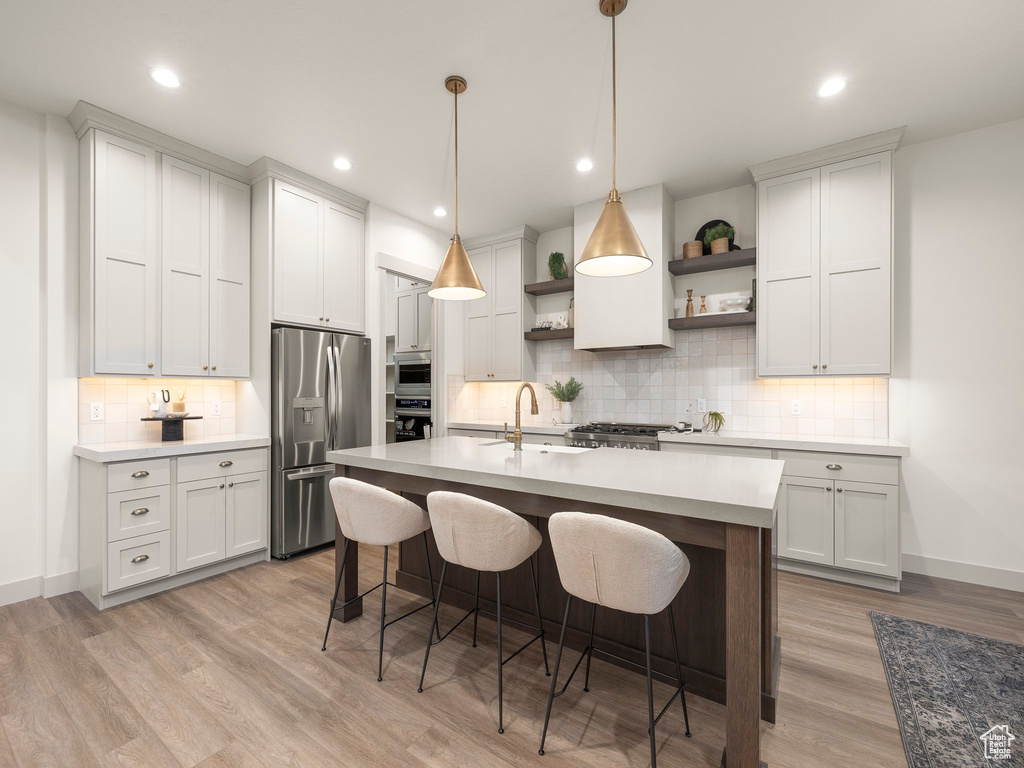 Kitchen with tasteful backsplash, white cabinets, a kitchen island with sink, light hardwood / wood-style floors, and appliances with stainless steel finishes