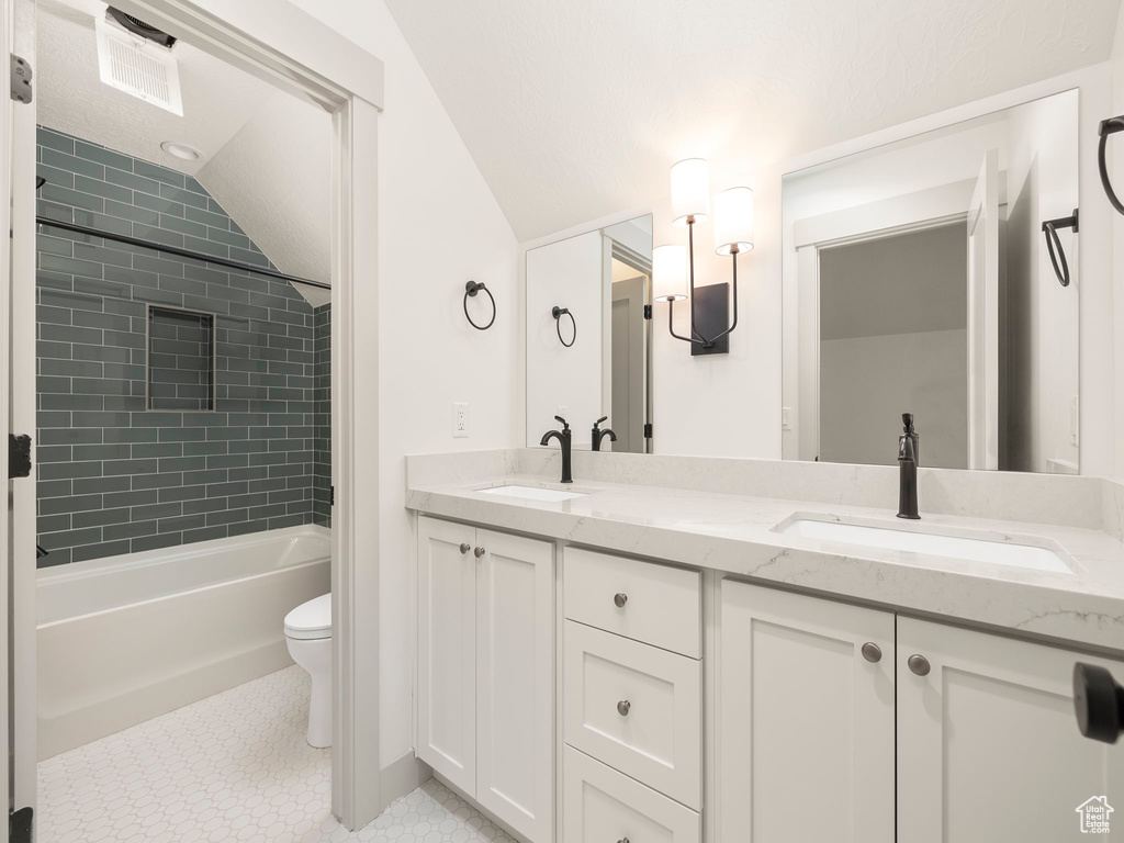 Full bathroom featuring vaulted ceiling, double vanity, tile patterned flooring, tiled shower / bath, and toilet