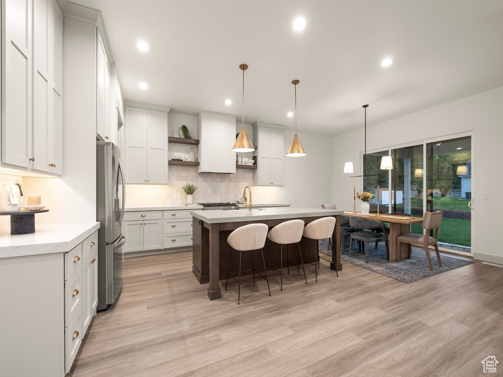 Kitchen featuring white cabinets, decorative light fixtures, decorative backsplash, light wood-type flooring, and stainless steel refrigerator with ice dispenser
