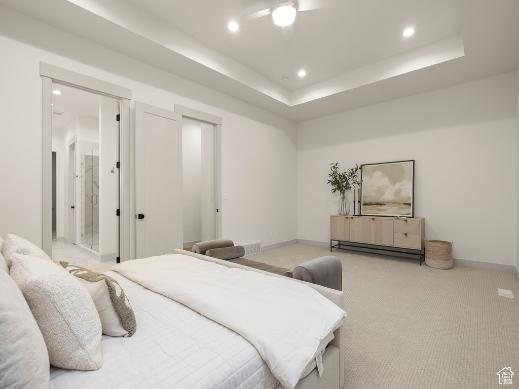 Bedroom with a tray ceiling, light colored carpet, ensuite bath, and ceiling fan