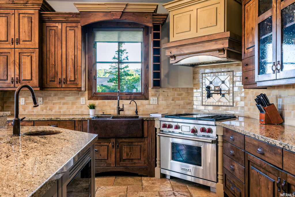 Kitchen with premium range hood, sink, backsplash, light tile floors, and designer range