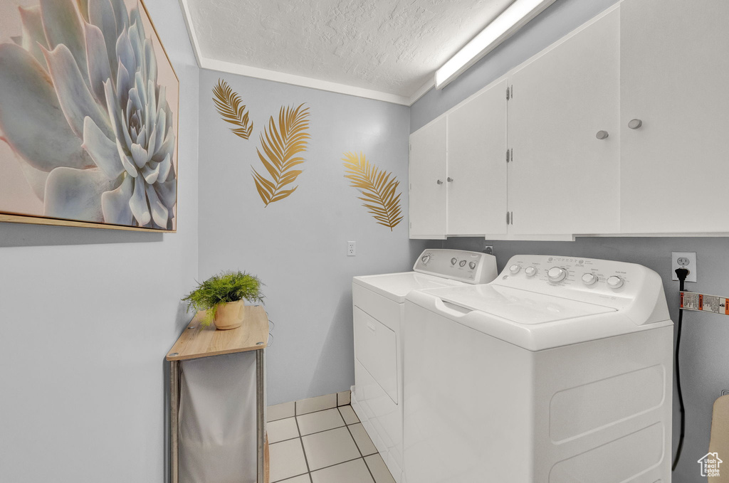 Washroom featuring ornamental molding, washing machine and clothes dryer, light tile flooring, cabinets, and a textured ceiling