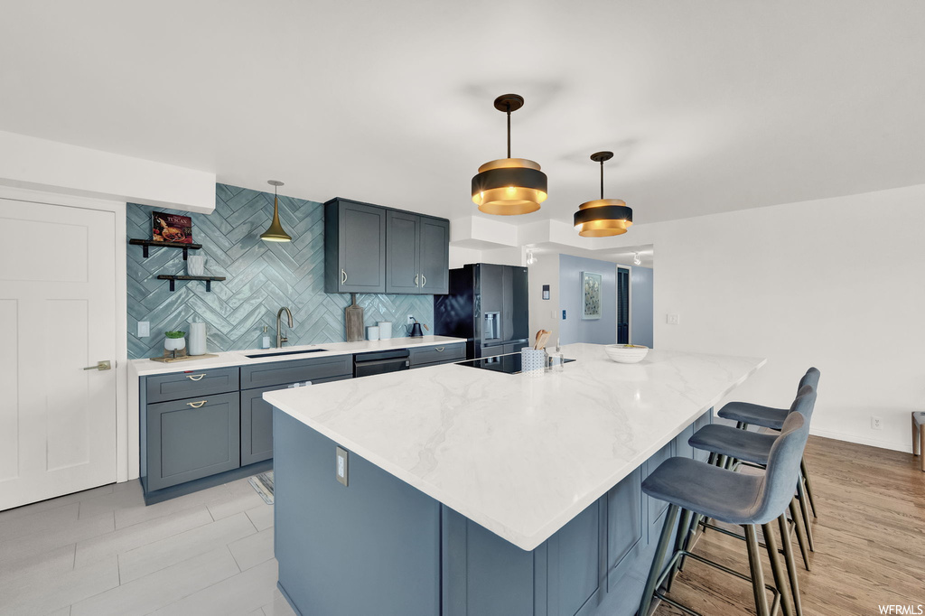 Kitchen featuring sink, backsplash, pendant lighting, light stone counters, and a kitchen breakfast bar