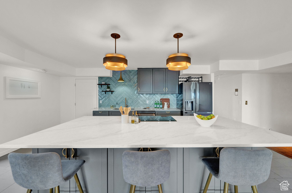 Kitchen featuring decorative light fixtures, tasteful backsplash, a kitchen island, light tile floors, and stainless steel refrigerator with ice dispenser