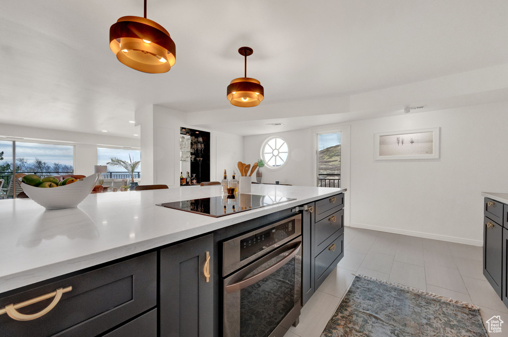 Kitchen featuring light tile floors, stainless steel oven, black electric cooktop, and pendant lighting