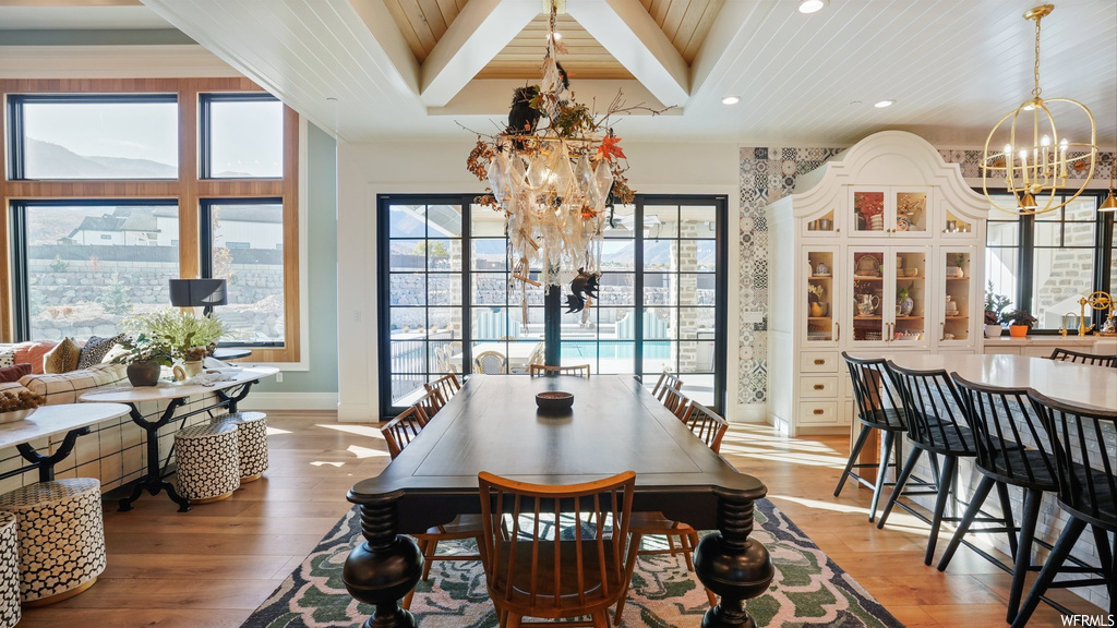 Dining space with light hardwood / wood-style floors, beam ceiling, and a notable chandelier