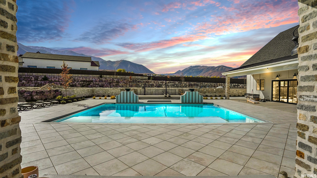 Pool at dusk featuring a mountain view and a patio