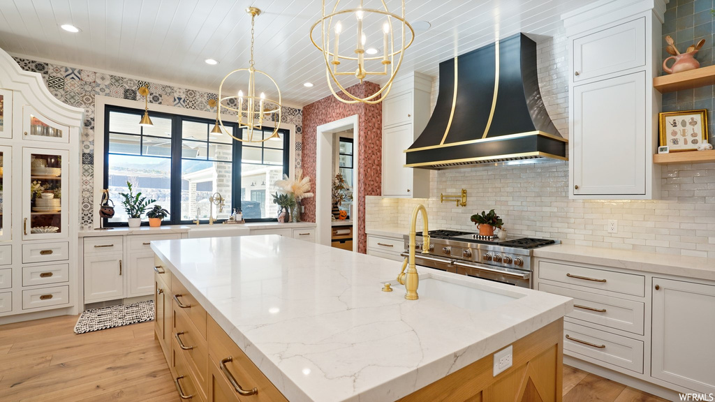 Kitchen with a chandelier, premium range hood, light hardwood / wood-style flooring, and white cabinetry