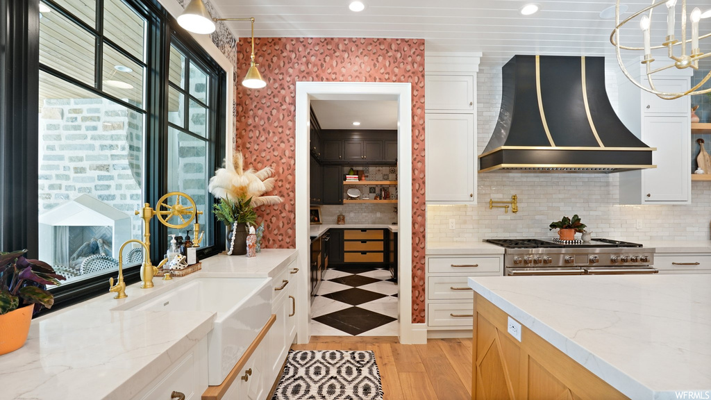 Kitchen featuring premium range hood, light wood-type flooring, hanging light fixtures, and white cabinetry