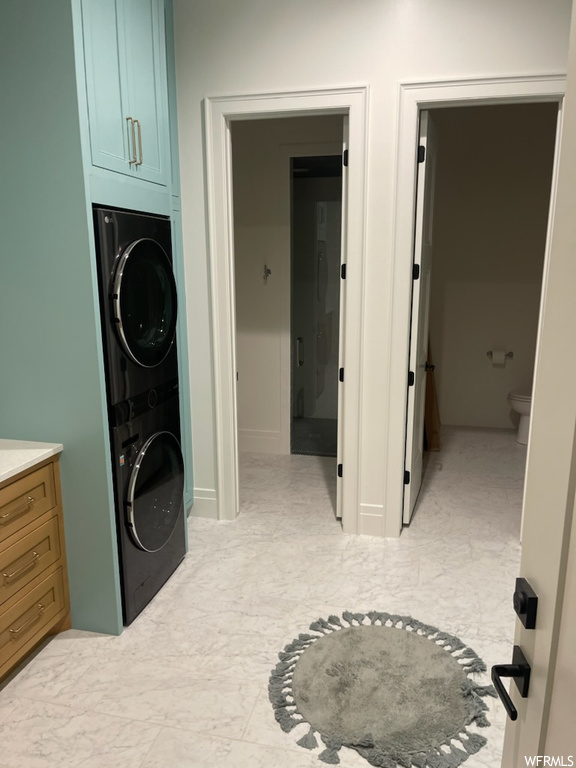 Washroom featuring stacked washer / dryer, light tile floors, and cabinets