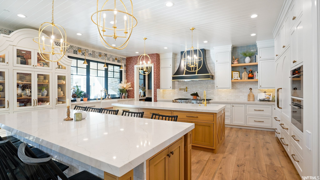 Kitchen featuring a kitchen island, an inviting chandelier, white cabinetry, custom exhaust hood, and decorative light fixtures
