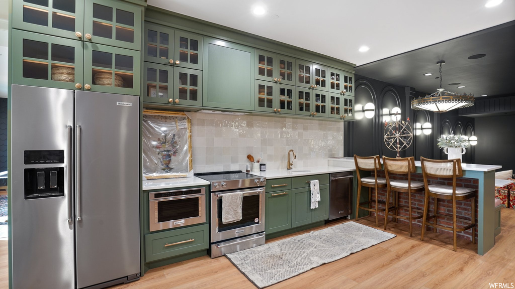 Kitchen featuring stainless steel appliances, hanging light fixtures, backsplash, and green cabinets