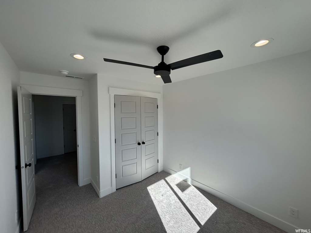 Unfurnished bedroom with ceiling fan, dark carpet, and a closet