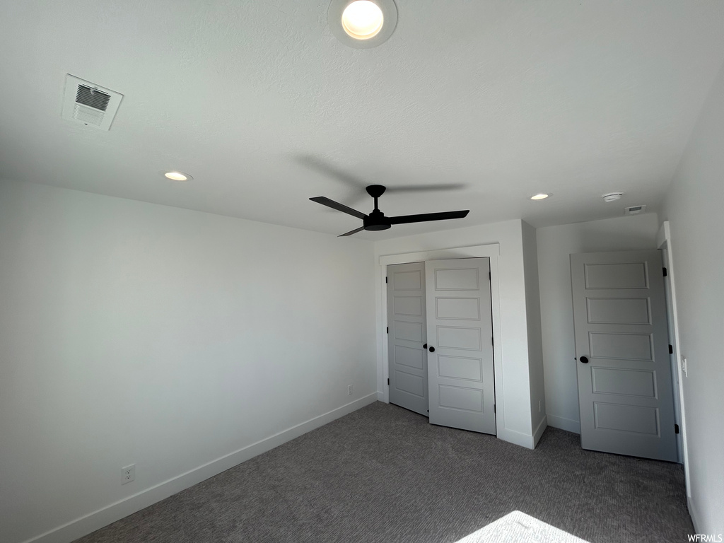 Unfurnished bedroom featuring ceiling fan, dark colored carpet, and a closet