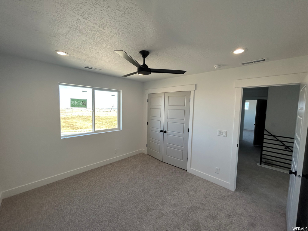 Unfurnished bedroom featuring ceiling fan, dark carpet, a closet, and a textured ceiling