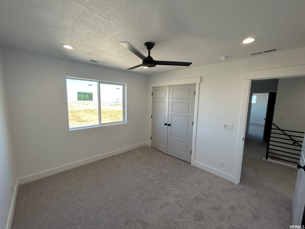 Unfurnished bedroom with ceiling fan, dark colored carpet, a closet, and a textured ceiling