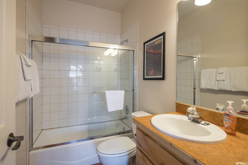 Full bathroom with vanity, bath / shower combo with glass door, and toilet