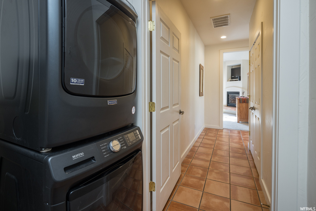 Laundry room featuring stacked washer / dryer, a fireplace, and light tile floors
