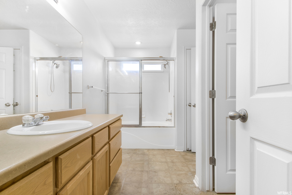 Bathroom with tile floors, vanity with extensive cabinet space, and shower / bath combination with glass door