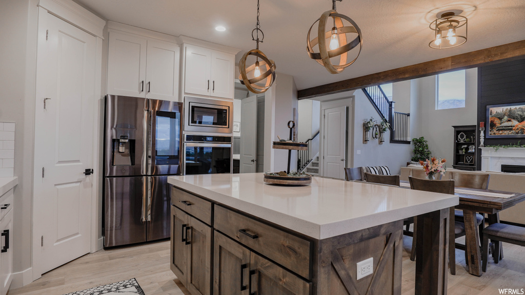 Kitchen with light hardwood / wood-style flooring, appliances with stainless steel finishes, a kitchen island, white cabinetry, and pendant lighting