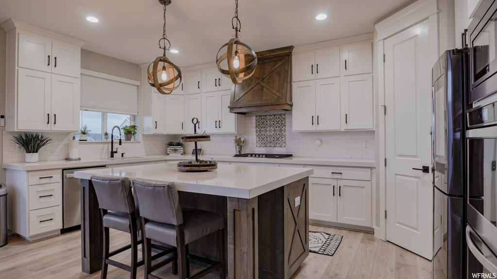 Kitchen featuring light hardwood / wood-style floors, tasteful backsplash, premium range hood, and a kitchen island