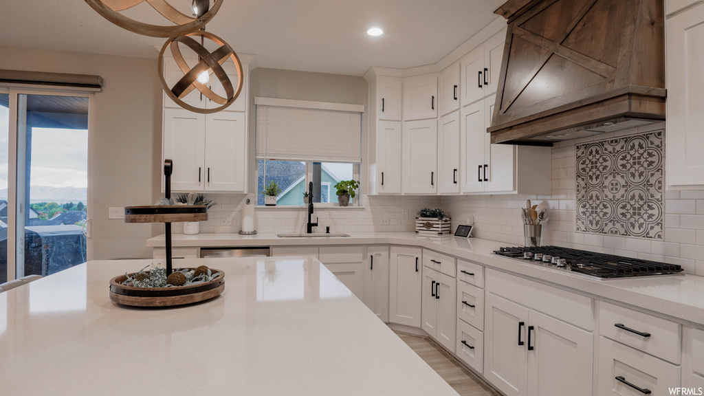 Kitchen featuring premium range hood, sink, backsplash, pendant lighting, and white cabinetry