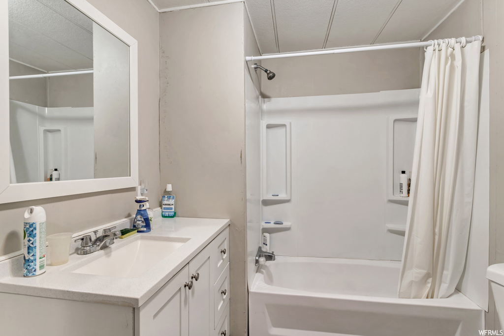 Full bathroom with shower / tub combo with curtain, oversized vanity, a textured ceiling, and toilet