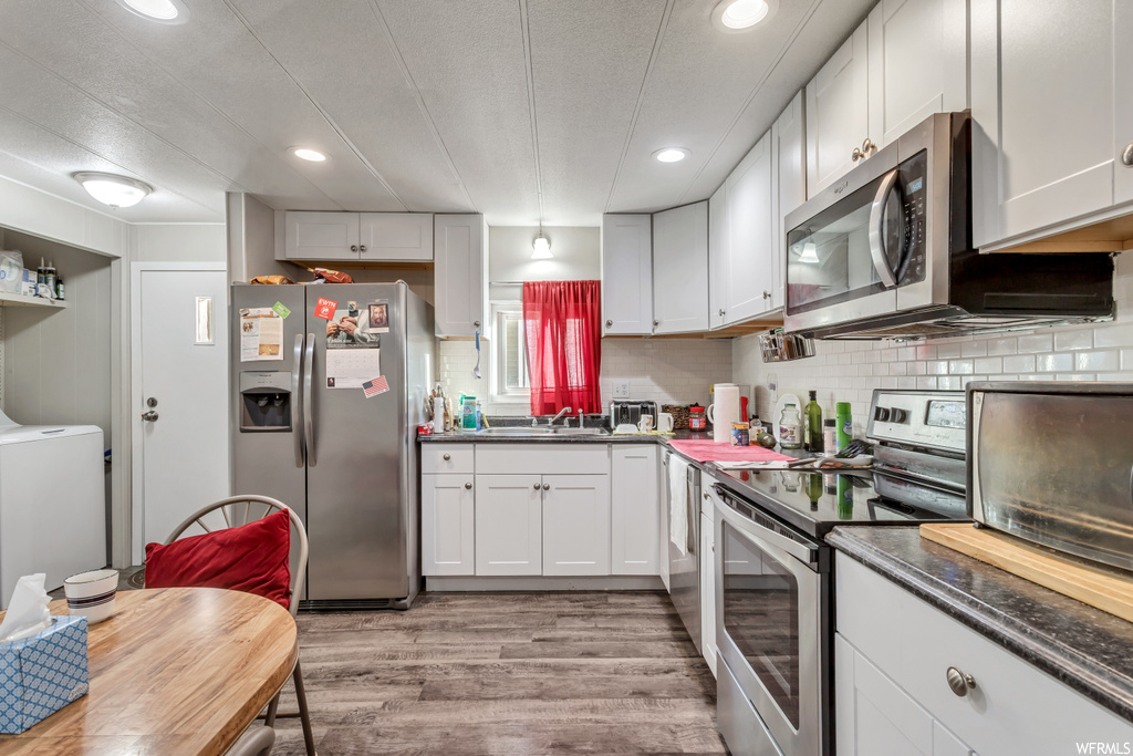 Kitchen featuring light hardwood / wood-style floors, stainless steel appliances, hanging light fixtures, white cabinets, and washer / clothes dryer