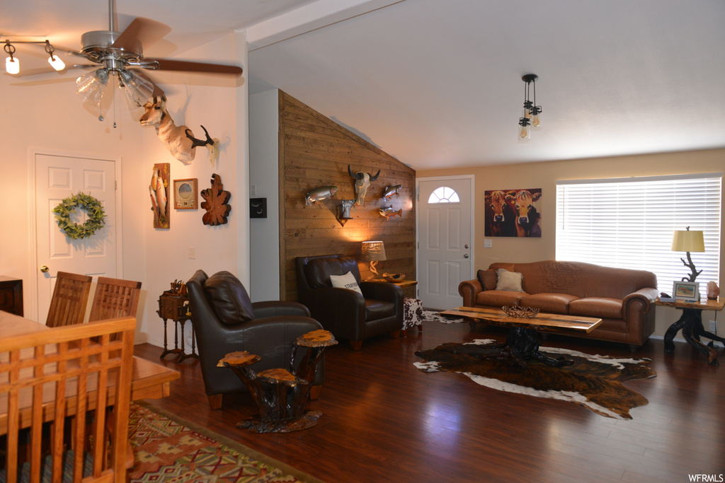Living room with vaulted ceiling, wood walls, ceiling fan, and dark wood-type flooring