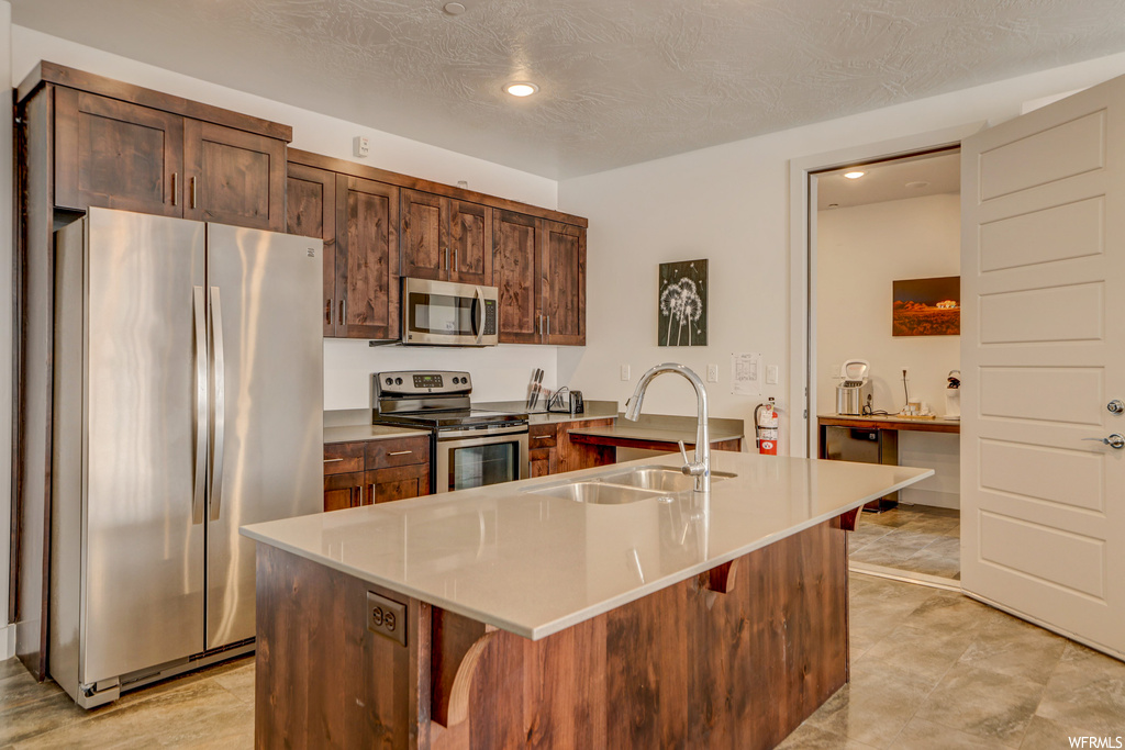 Kitchen with a center island with sink, sink, light tile floors, a breakfast bar, and stainless steel appliances