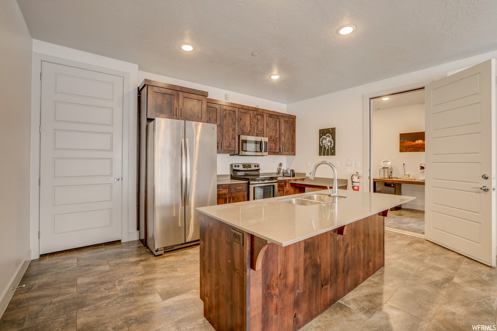 Kitchen featuring a center island with sink, sink, stainless steel appliances, a kitchen breakfast bar, and light tile flooring