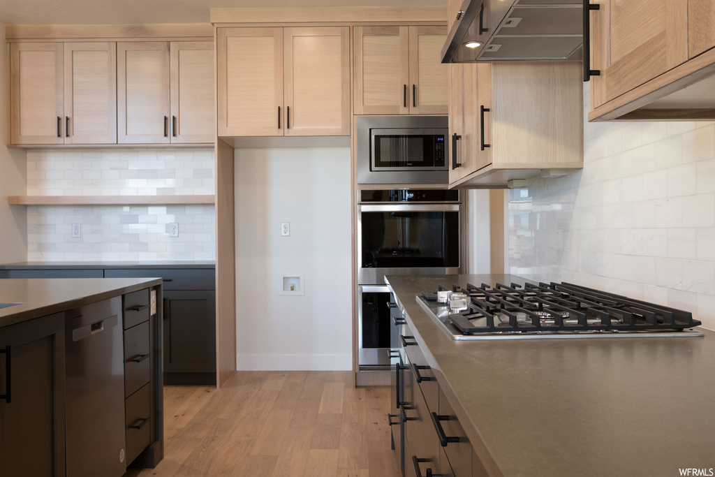 Kitchen featuring stainless steel appliances, light wood-type flooring, wall chimney exhaust hood, and tasteful backsplash