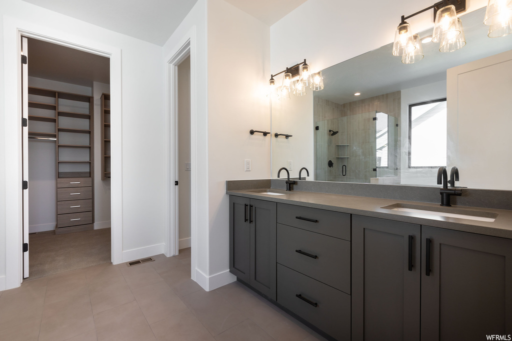 Bathroom with dual vanity, an enclosed shower, an inviting chandelier, and tile flooring