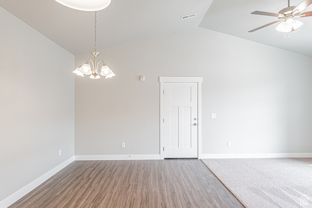 Empty room featuring ceiling fan with notable chandelier, dark hardwood / wood-style flooring, and vaulted ceiling