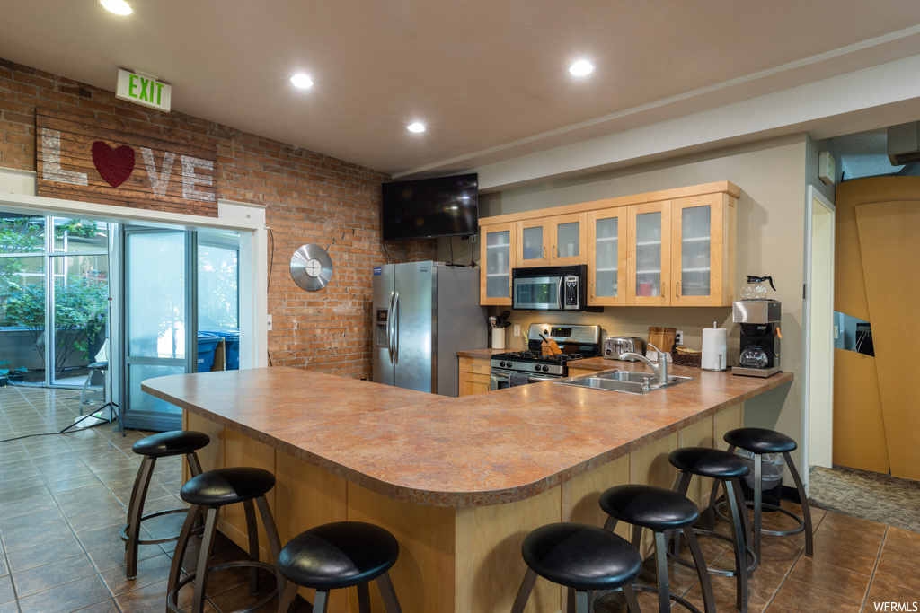 Kitchen featuring a kitchen breakfast bar, dark tile floors, appliances with stainless steel finishes, and brick wall