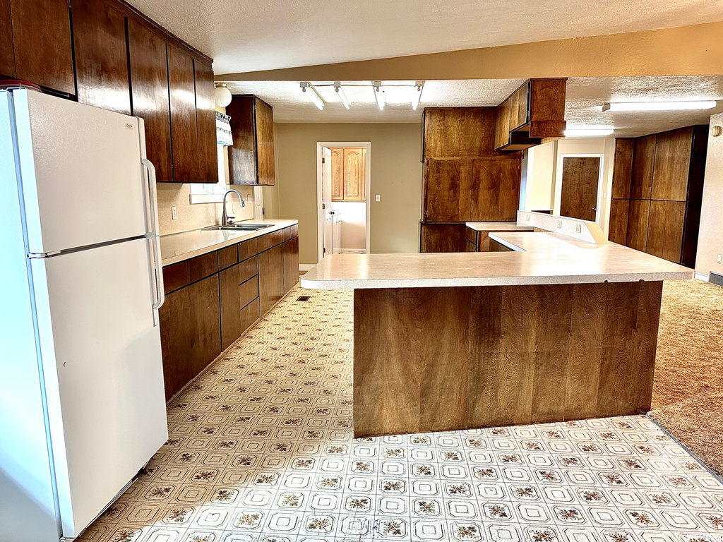 Kitchen featuring sink, rail lighting, light tile floors, white refrigerator, and kitchen peninsula