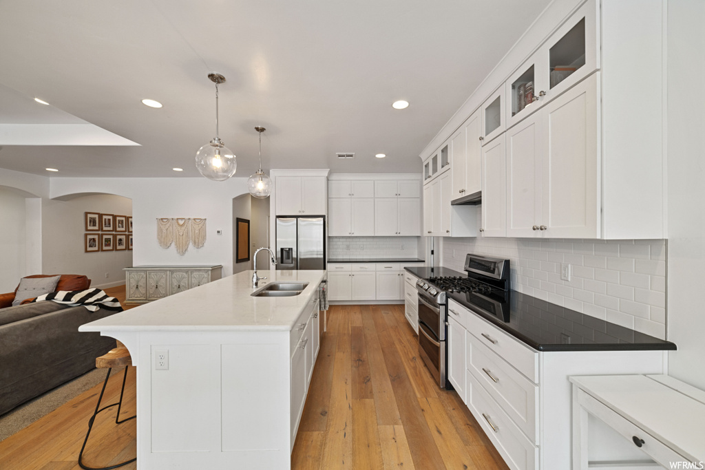 Kitchen featuring stainless steel appliances, light wood-type flooring, tasteful backsplash, and white cabinetry