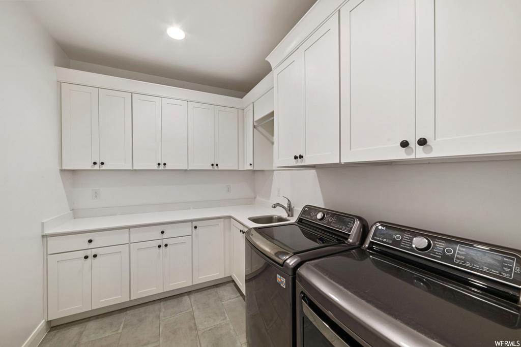 Laundry area featuring sink, separate washer and dryer, cabinets, and light tile floors