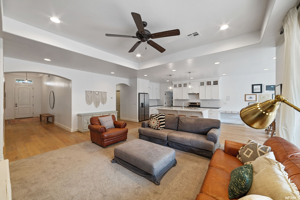Living room with a tray ceiling, light wood-type flooring, and ceiling fan