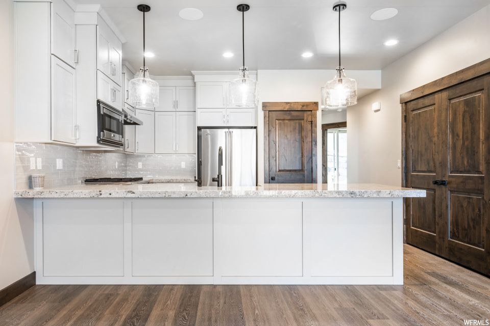 Kitchen with stainless steel appliances, decorative light fixtures, white cabinets, and light hardwood / wood-style flooring